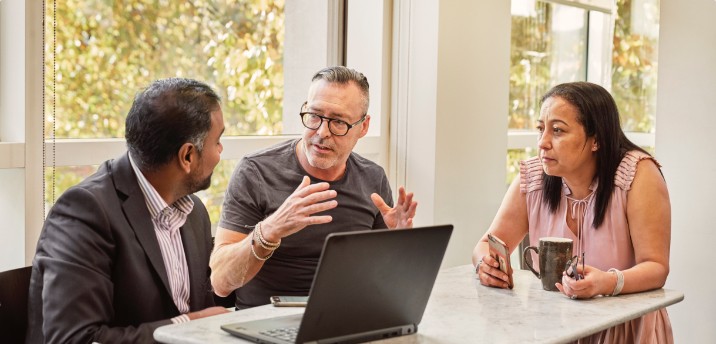 Three business-people hold a discussion at a table.